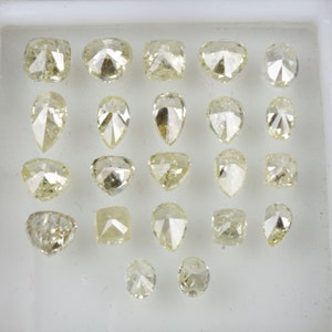 May include: A collection of 20 loose diamonds in various shapes and sizes, displayed in a white tray. The diamonds are all a pale yellow color.