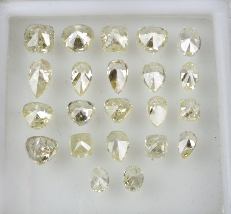 May include: A collection of 20 loose diamonds in various shapes and sizes, displayed in a white tray. The diamonds are all a pale yellow color.