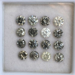 May include: A collection of 15 round, faceted, gray diamonds in a white box. The diamonds are arranged in three rows of five.