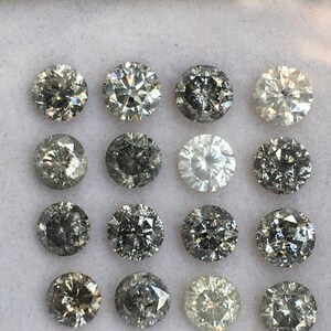 May include: A collection of 16 round, faceted, grey diamonds in a white box. The diamonds are arranged in four rows of four.
