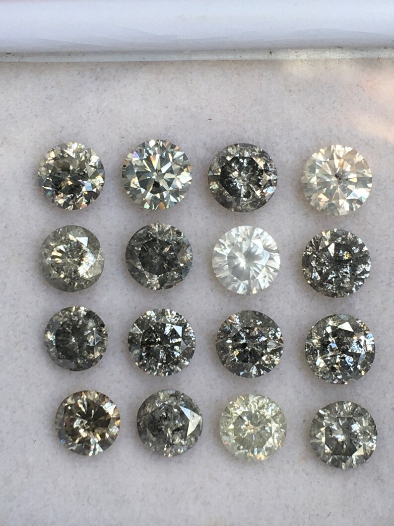 May include: A collection of 16 round, faceted, grey diamonds in a white box. The diamonds are arranged in four rows of four.