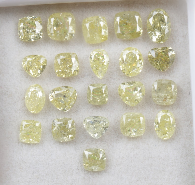 May include: A collection of 21 loose yellow diamonds of various shapes and sizes, displayed in a white tray.