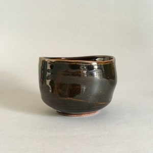 May include: A dark brown ceramic teacup with a slightly uneven rim and a glossy finish.