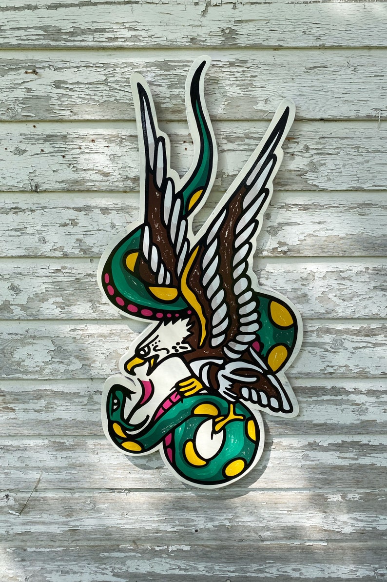 May include: A green and yellow snake wrapped around a brown and white eagle with pink accents. The eagle is attacking the snake. The image is a traditional tattoo design.