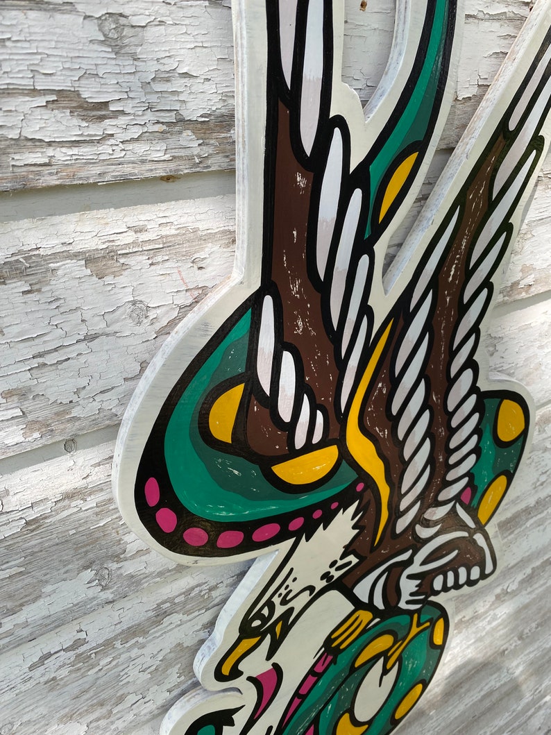 May include: A green, yellow, and pink eagle with wings outstretched, holding a green snake in its talons. The eagle is depicted in a traditional American tattoo style.