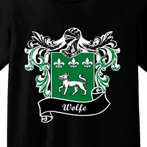 Könnte beinhalten: Schwarzes T-Shirt mit einem Familienwappen-Design. Das Wappen zeigt einen grünen Schild mit einem weißen Hund, drei Lilien und dem Namen "Wolfe" auf einem Banner. Das Wappen ist von grünen und weißen dekorativen Elementen umrahmt.