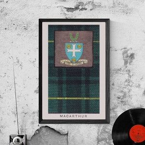 Op de afbeelding: Een ingelijste print van een tartanpatroon met een wapenschild en de tekst "MacArthur" onderaan. De print hangt aan een grijze, getextureerde muur met een vintage radio en een zwarte vinylplaat op een zwarte plank eronder.