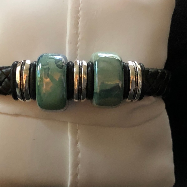 Pulsera de cuero de regaliz negro con cuentas de cerámica jaspeada verde azulado iridiscente múltiple y separadores de plata envejecida sobre cuero trenzado.