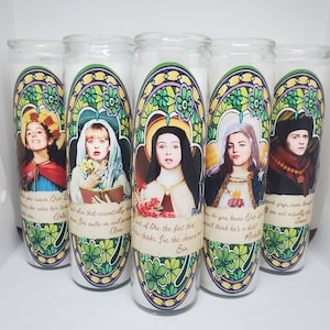 May include: Five glass candle holders with colorful stained glass designs featuring different characters. Each candle holder has a quote and a name at the bottom. The quotes are: "You know our Lord", "She's that essentially", "I sort of like the fact that", "How do you know Our Lord", "I'm not gay, even though". The names are: "Michelle", "James", "Erin", "Clare", "Oula".