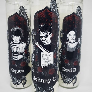 May include: Three glass candle jars with black and white illustrations of characters from the movie 'The Shining'. The candles are white and the jars have black and red accents. The text on the jars reads 'Squee', 'Johnny C', and 'Devi D'.