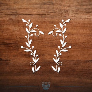 May include: Two white floral branch designs with leaves and berries are displayed against a dark brown wood grain background. The branches are symmetrical, with curved stems and delicate details, creating a natural, decorative element.