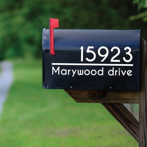 May include: A black mailbox with the address 15923 and the street name Marywood drive in white lettering. The mailbox has a red flag and is mounted on a wooden post.