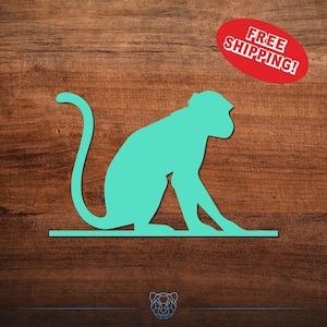 May include: A turquoise monkey silhouette sits on a horizontal line against a wood grain background. A red oval with the words "FREE SHIPPING!" is in the upper right corner. The monkey is in a seated position with its tail curved.