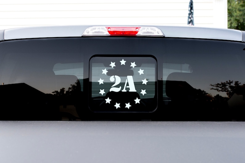 May include: A white vinyl sticker with a circle of stars surrounding the text "2A" on a black truck window.