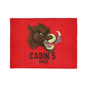 Könnte beinhalten: Rote Fleece-Decke mit einem Cartoon-Bild eines Eberkopfes mit einem großen Hauer. Der Text "CABIN 5 ARES" ist unter dem Bild gedruckt.