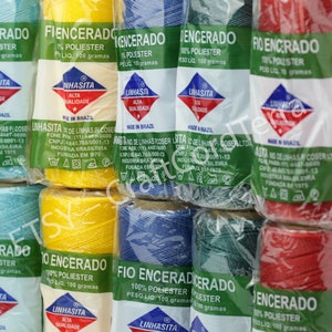May include: Assortment of spools of waxed thread in various colors, including blue, yellow, red, and green. Each spool is labeled "Fio Encerado" and "100% Polyester" with the weight listed as 100 grams. The label also includes the brand name "Linhasita" and the text "Alta Qualidade" (High Quality) and "Made in Brazil".