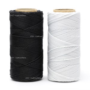 May include: Two spools of cord, one black and one white. The spools are made of cardboard and have a label that says "ETSY - CraftCord Terra".