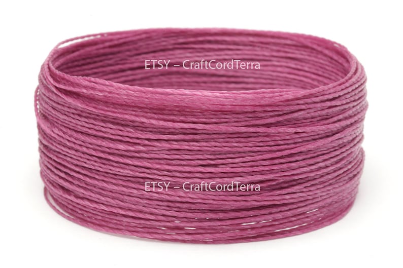 May include: A close-up of a spool of pink waxed cotton cord. The cord is wound tightly and is ready to be used for crafting projects.