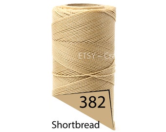 May include: A spool of Shortbread-colored macrame cord. The cord is tightly wound around a cardboard core. A tan label with the number 382 is visible at the bottom. The cord is a neutral beige color.