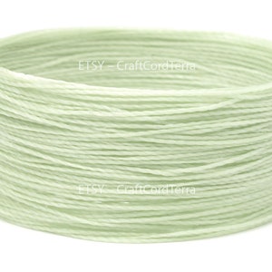 May include: A spool of pale green waxed cotton cord. The cord is wound tightly and is ready to be used for crafting projects.