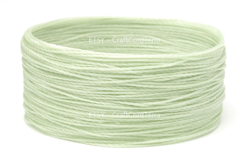 May include: A spool of pale green waxed cotton cord. The cord is wound tightly and is ready to be used for crafting projects.