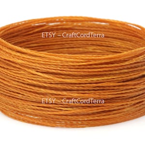 May include: A close-up of a spool of orange waxed cord. The cord is tightly wound and has a slight sheen. The text "ETSY - CraftCordTerra" is visible on the spool.