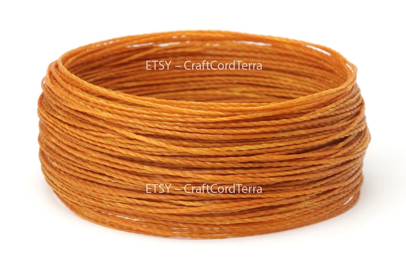 May include: A close-up of a spool of orange waxed cord. The cord is tightly wound and has a slight sheen. The text "ETSY - CraftCordTerra" is visible on the spool.