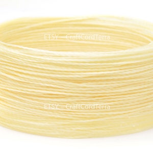 May include: A close-up of a spool of cream-colored waxed cotton cord. The cord is wound tightly and is ready to be used for crafting projects.