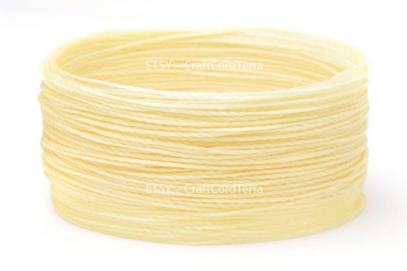 May include: A close-up of a spool of cream-colored waxed cotton cord. The cord is wound tightly and is ready to be used for crafting projects.
