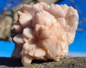 May include: A cluster of pink quartz crystals with a rough, natural texture. The crystals are arranged in a cluster, with some of the points facing upwards. The crystals are a light pink color, and they have a slightly translucent appearance.
