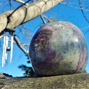May include: A large, round, polished stone with a swirling pattern of green, purple, and white. The stone is resting on a weathered wooden surface.