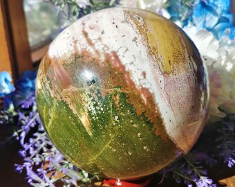 May include: A green, yellow, white, and pink sphere made of polished stone. The sphere is sitting on a red stand.
