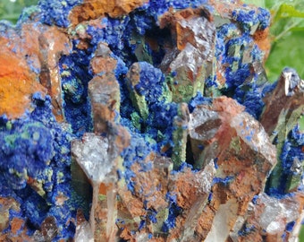 May include: A cluster of quartz crystals with a blue and green mineral, possibly azurite and malachite, embedded in the center. The crystals are clear and have a rough, natural texture.