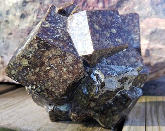 May include: A large, dark brown, faceted garnet crystal with a rough, textured surface. The crystal has a geometric shape with many facets.