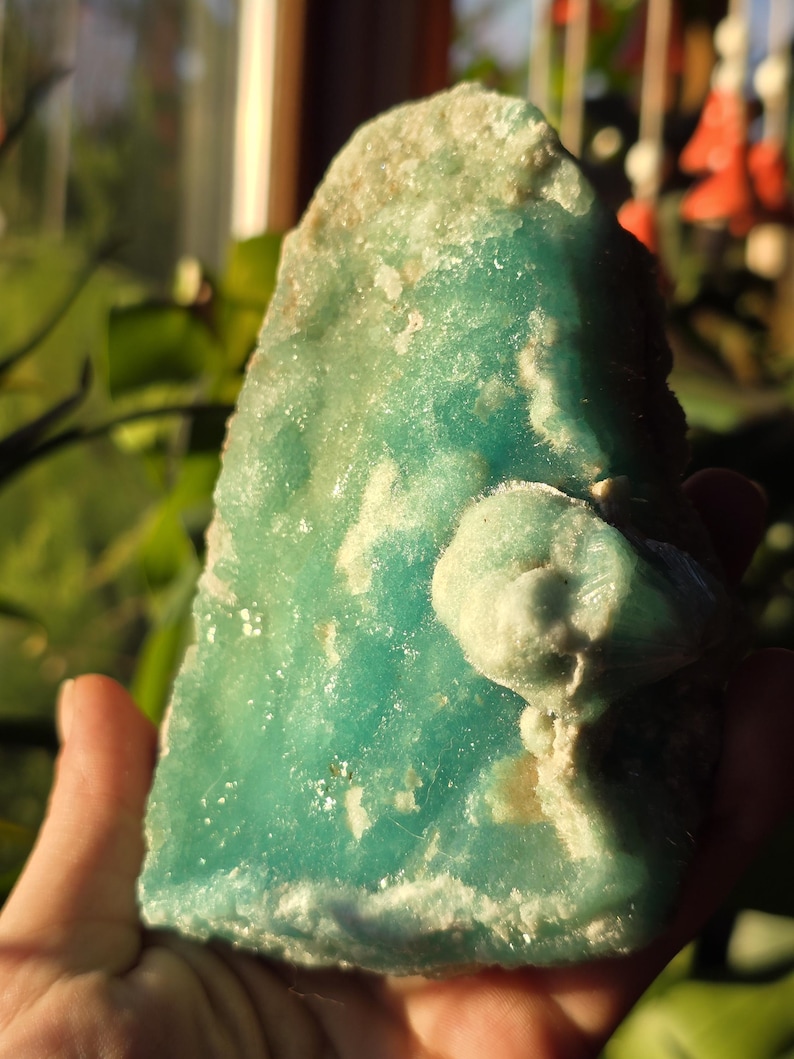 Puede incluir: Una mano sostiene un esp&eacute;cimen mineral grande con bordes &aacute;speros. La piedra es principalmente de color turquesa vibrante con parches blanquecinos y beige. La superficie tiene una textura cristalina y la forma general es irregular.