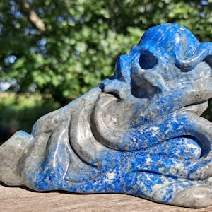 Puede incluir: Una escultura de calavera de lapislázuli azul y gris tallada en forma de figura agachada. La escultura tiene un diseño detallado e intrincado.