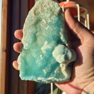 Puede incluir: Un esp&eacute;cimen mineral de color turquesa vibrante con una superficie rugosa y texturizada. La piedra tiene una estructura cristalina y una capa superior m&aacute;s clara, casi blanca y costrosa. Una peque&ntilde;a formaci&oacute;n redondeada sobresale del cuerpo principal de la piedra.