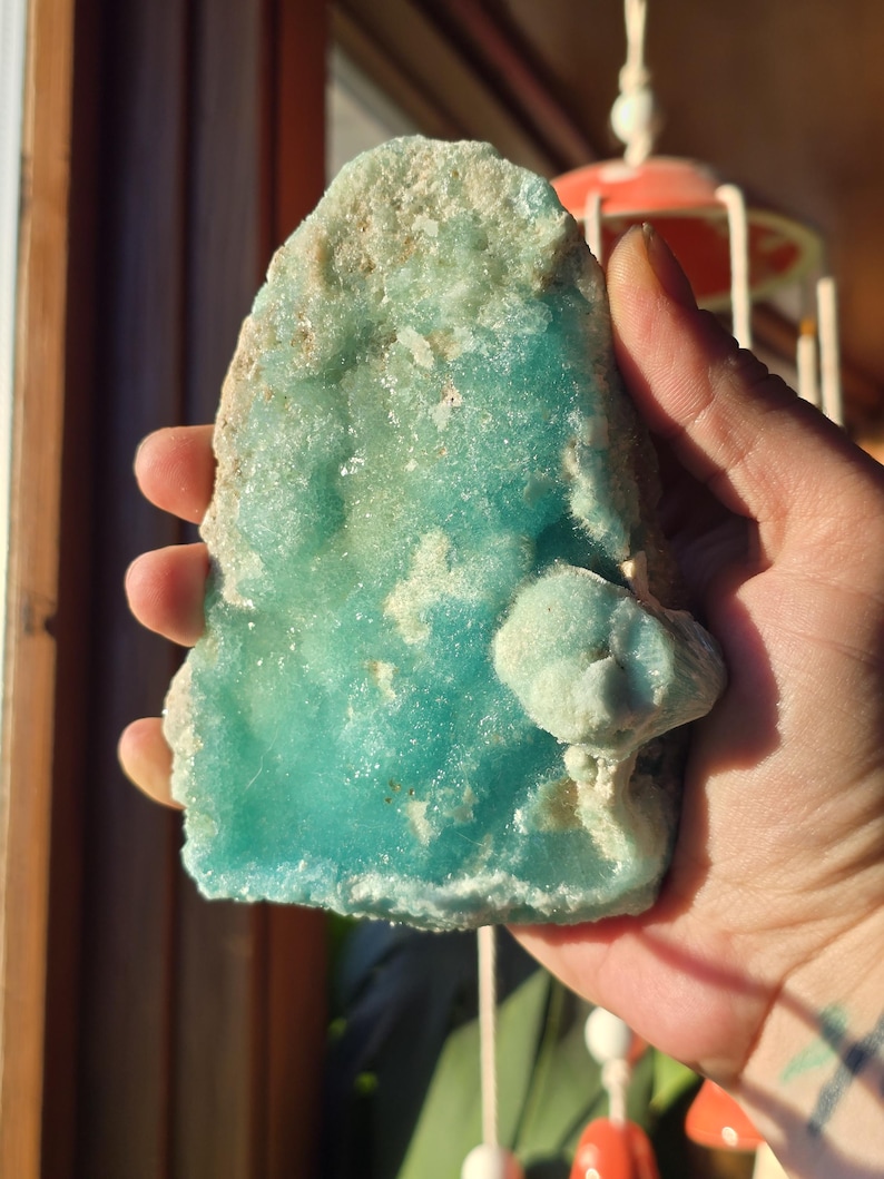 Puede incluir: Un esp&eacute;cimen mineral de color turquesa vibrante con una superficie rugosa y texturizada. La piedra tiene una estructura cristalina y una capa superior m&aacute;s clara, casi blanca y costrosa. Una peque&ntilde;a formaci&oacute;n redondeada sobresale del cuerpo principal de la piedra.