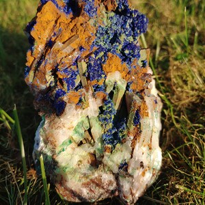 May include: A cluster of blue azurite, green malachite, and clear quartz crystals. The crystals are embedded in a matrix of brown iron oxide.