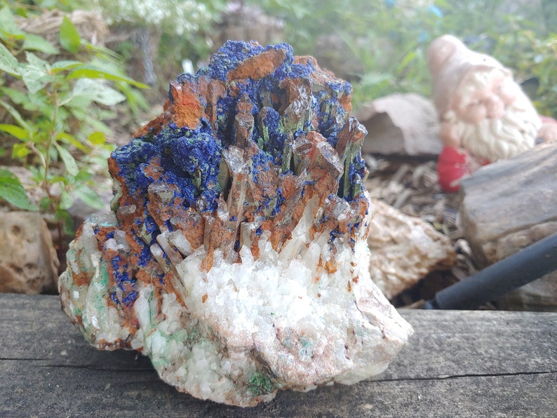 May include: A cluster of crystals with a mix of blue, green, white, and brown colors. The crystals are arranged in a natural formation, with some pointing upwards and others pointing downwards.