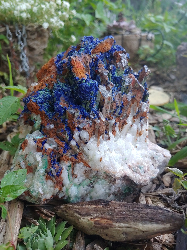 May include: A cluster of white quartz crystals with blue azurite and green malachite inclusions. The crystals are arranged in a natural formation, with some of the quartz crystals pointing upwards.