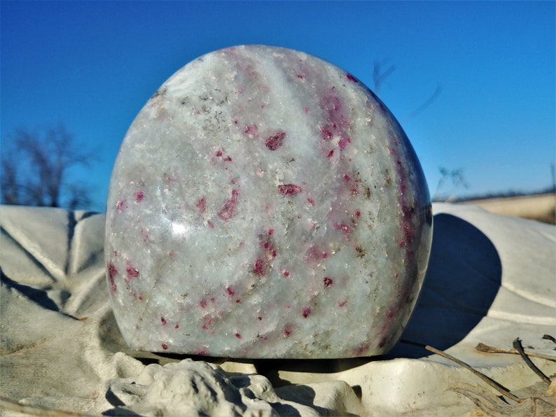 May include: A smooth, white and gray sphere with red and pink inclusions. The sphere is polished and has a glossy finish.