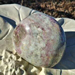 May include: A polished, round, white and pink gemstone with a smooth, shiny surface. The gemstone has a swirling pattern of pink and white.