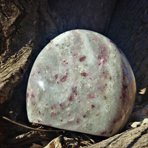 May include: A smooth, white, and gray polished stone with red inclusions. The stone is shaped like an egg and is resting on a piece of wood.