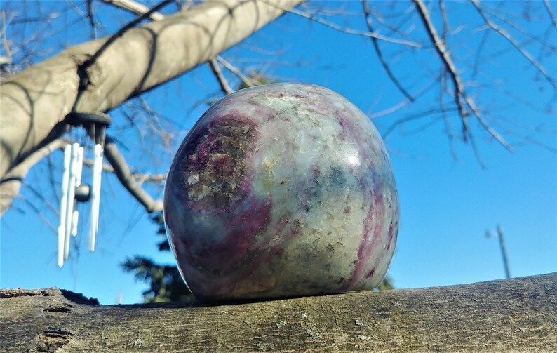 May include: A large, round, polished stone with a swirling pattern of green, purple, and white. The stone is resting on a weathered wooden surface.