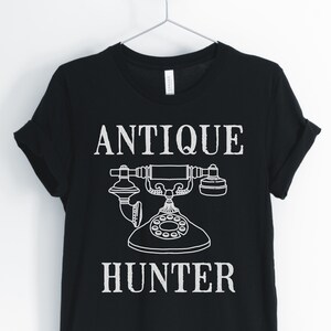 May include: Black t-shirt with white text that reads "Antique Hunter" and a vintage rotary phone graphic.