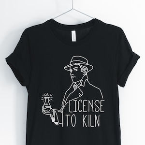 May include: Black t-shirt with a white graphic of a man in a fedora holding a beaker with the text "License to Kiln".