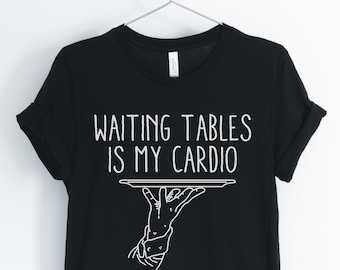 Może przedstawiać: Czarny T-shirt z białym tekstem, który brzmi "Waiting tables is my cardio" i grafiką dłoni trzymającej tacę.