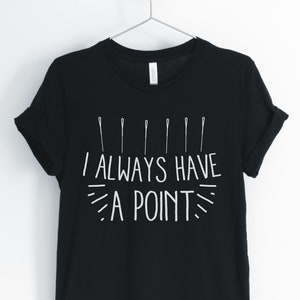 May include: Black t-shirt with the text "I ALWAYS HAVE A POINT" in white, along with a graphic of several straight pins. The shirt is hanging on a metal hanger against a white background.