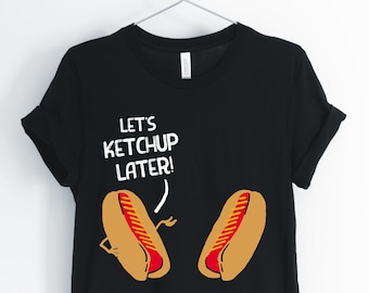 May include: Black t-shirt with a white graphic of two hot dogs with the text "Let's Ketchup Later!"
